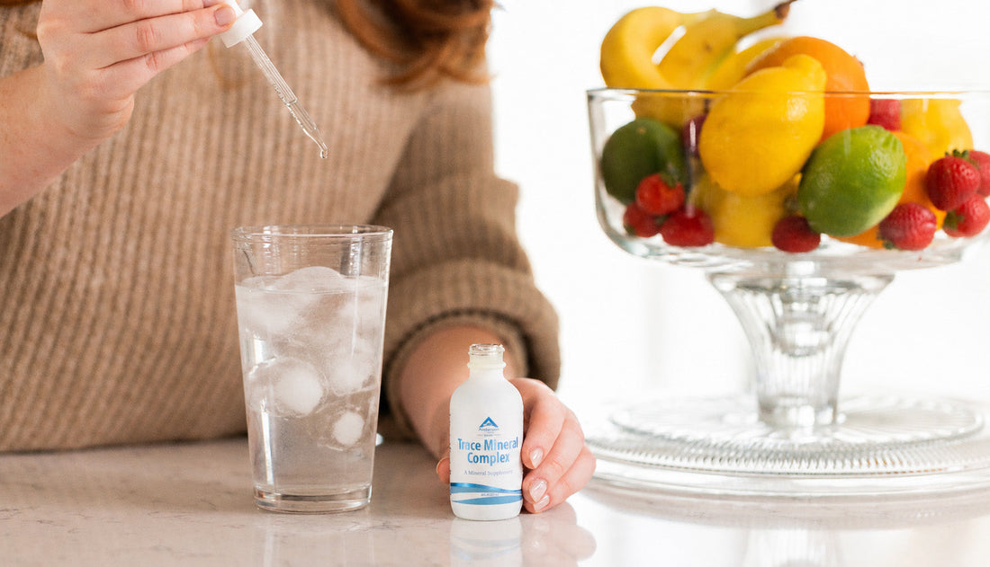 Hand holding Anderson Trace Mineral Complex dropper above a glass of water